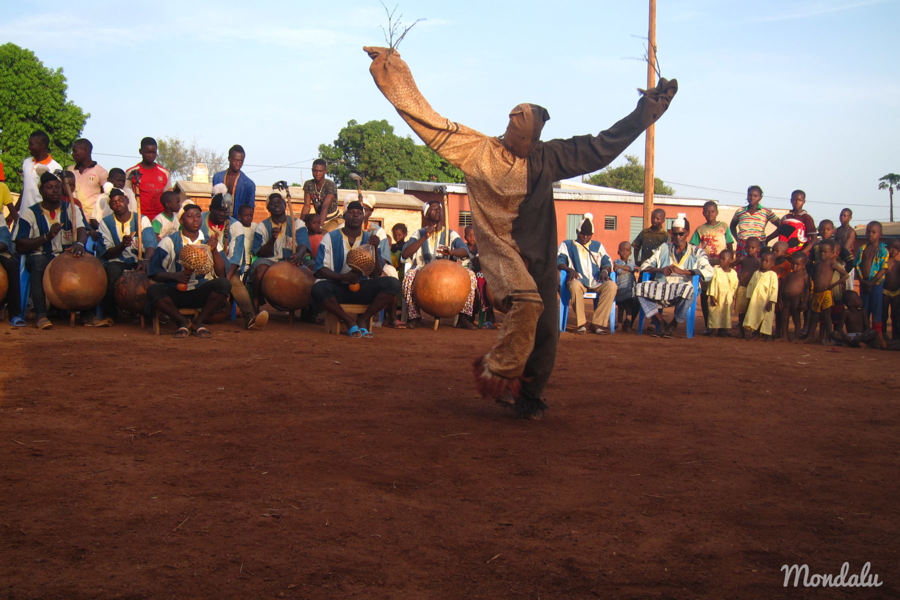 Photo de la danse Boloye, avec un danseur en habit de panthère levant les bras devant l'ensemble des musiciens